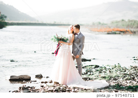 Elegant stylish happy blonde bride and gorgeous groom on the background of a beautiful river in the mountains 97540711