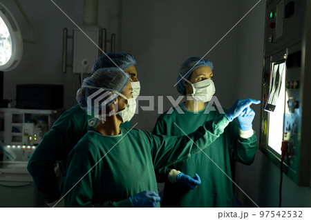 Three diverse surgeons preparing for operation, discussing x-ray in operating theatre Three diverse surgeons preparing for operation, discussing x-ray in operating theatre 97542532