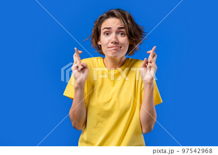 Pretty woman praying with crossed fingers on blue background. Lady begs someone satisfy her desires 97542968