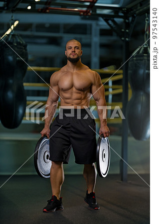 Athletic man with naked torso holding black plates in the gym 97543140