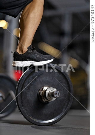 Muscular leg of a bodybuilder in a black sneaker on the gym 97543147