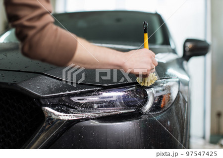 Close up photo of hands of auto service male worker in black protective gloves cleaning car hood 97547425