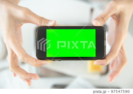closeup hand holding smartphone top view in restaurant with blank space green screen colored closeup hand holding smartphone top view in restaurant with blank space green screen colored 97547590