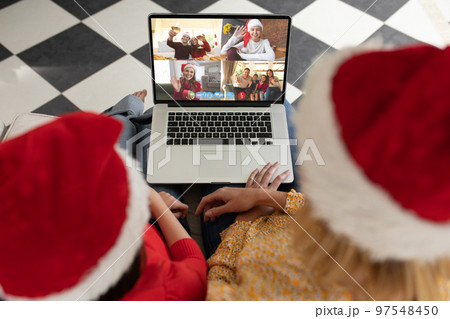 Caucasian mother and daughter in santa hats on christmas laptop video call with diverse friends 97548450