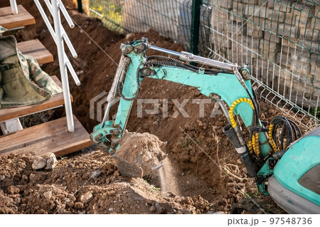 Mini excavator digs a trench to lay pipes. Close up of an excavator digging a deep trench. An excavator digs a trench in the countryside to lay a water pipe. Slow motion Mini excavator digs a trench to lay pipes. Close up of an excavator digging a deep trench. An excavator digs a trench in the countryside to lay a water pipe. Slow motion 97548736