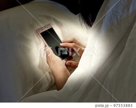 ベッドの中でスマホを見る人の手_スポットライト 97553883
