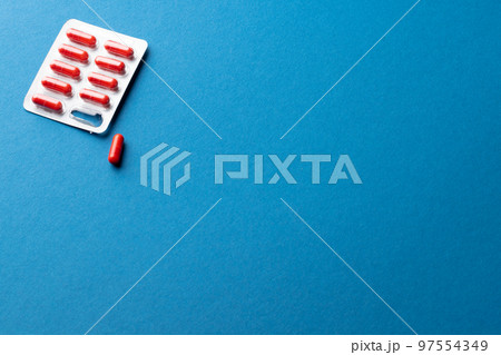 Composition of red pills in blister pack, and one pill out, on blue background with copy space Composition of red pills in blister pack, and one pill out, on blue background with copy space 97554349