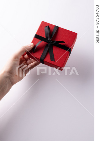 Vertical of hand giving red gift box tied with black ribbon, on white background with copy space 97554703