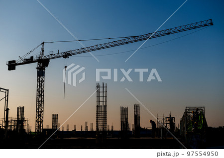 Industrial construction cranes and building silhouettes over sun at sunrise Industrial construction cranes and building silhouettes over sun at sunrise 97554950