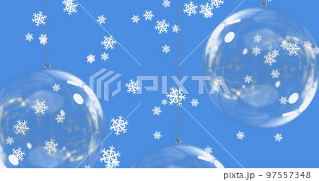 Snow falling over baubles on blue background 97557348