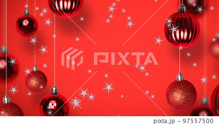 Image of snow falling over christmas bauble decorations on red background 97557500