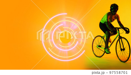 Biracial female athlete riding bike by illuminated circular pattern on yellow background Biracial female athlete riding bike by illuminated circular pattern on yellow background 97558701
