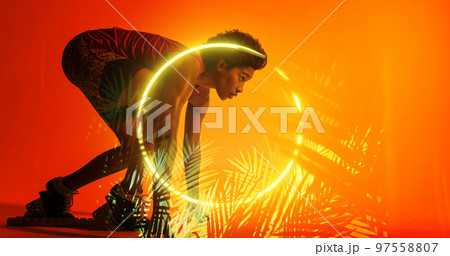Side view of biracial female athlete at starting position by illuminated plants and circle 97558807
