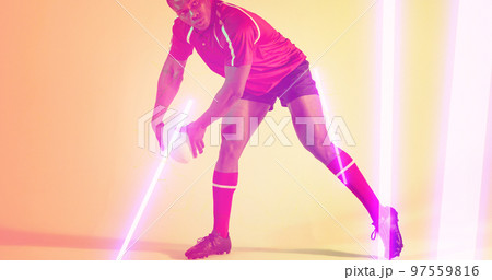 Low section of african american rugby player holding ball by glowing lights over beige background Low section of african american rugby player holding ball by glowing lights over beige background 97559816