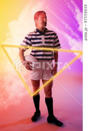 Illuminated triangle and smoke over thoughtful caucasian female player standing with rugby ball Illuminated triangle and smoke over thoughtful caucasian female player standing with rugby ball 97559939