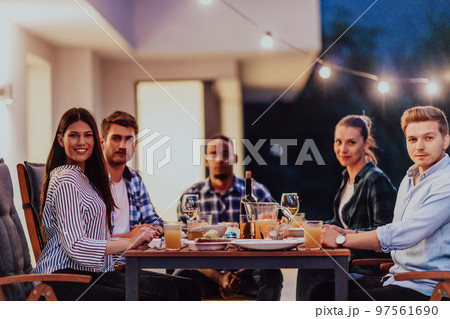 A group of young diverse people having dinner on the terrace of a modern house in the evening. Fun for friends and family. Celebration of holidays, weddings with barbecue. A group of young diverse people having dinner on the terrace of a modern house in the evening. Fun for friends and family. Celebration of holidays, weddings with barbecue. 97561690