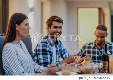 A group of young diverse people having dinner on the terrace of a modern house in the evening. Fun for friends and family. Celebration of holidays, weddings with barbecue. 97562245