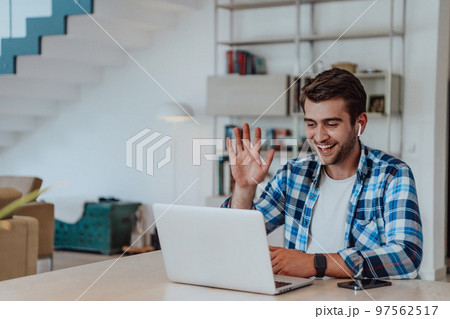 The man sitting at a table in a modern living room, with headphones using a laptop for business video chat, conversation with friends and entertainment The man sitting at a table in a modern living room, with headphones using a laptop for business video chat, conversation with friends and entertainment 97562517