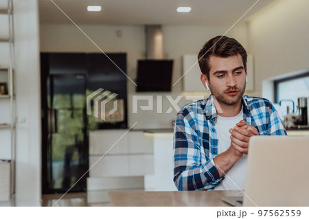 The man sitting at a table in a modern living room, with headphones using a laptop for business video chat, conversation with friends and entertainment 97562559