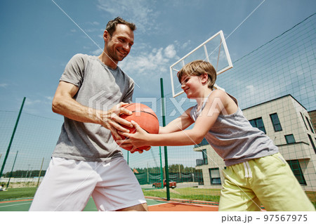 Side view father and son playing basketball together and smiling happily 97567975