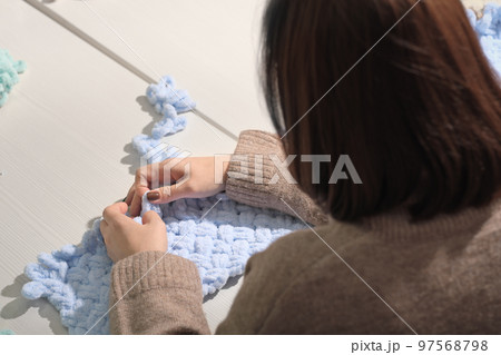 yarn being worked into a pattern with fingers. no needles knitting. back view of unrecognizable woman with fluffy thread. blue newborn baby blanket in progress. 97568798