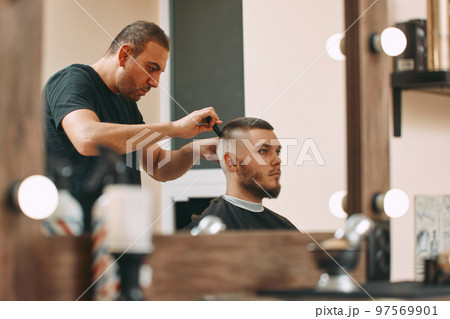 hairdresser does hairstyle with scissors in barber shop hairdresser does hairstyle with scissors in barber shop 97569901