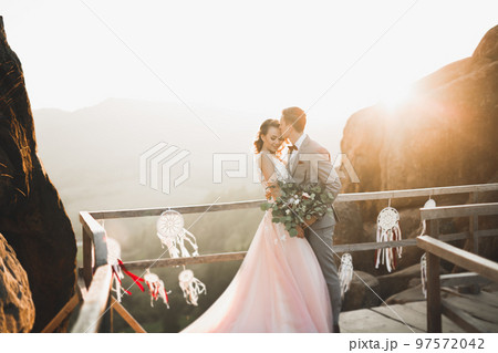 Young newly wed couple, bride and groom kissing, hugging on perfect view of mountains, blue sky Young newly wed couple, bride and groom kissing, hugging on perfect view of mountains, blue sky 97572042