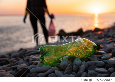 Earth day and global environmental pollution. Defocused silhouette of volunteer collects plastic bottles. Low angle view. Copy space. Coastal zone cleanup and conservation of ecology concept Earth day and global environmental pollution. Defocused silhouette of volunteer collects plastic bottles. Low angle view. Copy space. Coastal zone cleanup and conservation of ecology concept 97572887