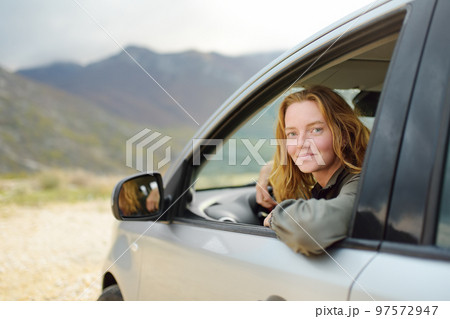 A young beautiful red-haired woman travels alone driving her car. A young beautiful red-haired woman travels alone driving her car. 97572947