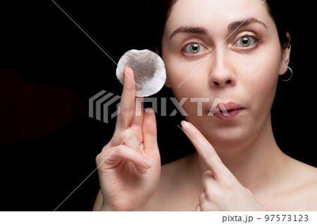 A beautiful girl is surprised and points the finger a cotton pad with makeup. Black background, copy space A beautiful girl is surprised and points the finger a cotton pad with makeup. Black background, copy space 97573123