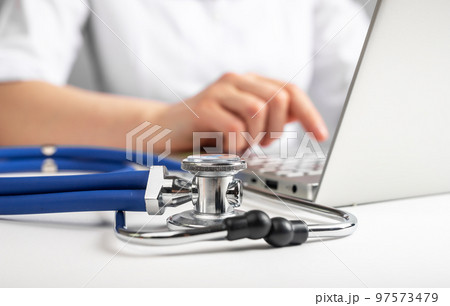 Doctor sitting at table with laptop and stethoscope. Online treatment of patients. Using computer for work in hospital. 97573479