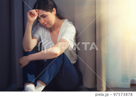 Portrait of a stressed crying woman, clutching her head and sitting on the floor. Copy space. Light from window. The concept of domestic violence Portrait of a stressed crying woman, clutching her head and sitting on the floor. Copy space. Light from window. The concept of domestic violence 97573878