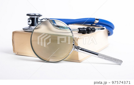 Book with stethoscope and magnifying glass. Medical education, search of information about medicine, health problems and treatment. Book with stethoscope and magnifying glass. Medical education, search of information about medicine, health problems and treatment. 97574371