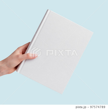 Hand holding book mockup on blue background. White cover template. Literature, education, reading concept. Hand holding book mockup on blue background. White cover template. Literature, education, reading concept. 97574789