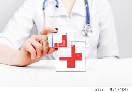 First aid. Cubes with red cross in doctor hands. Urgent medical care. Woman in lab coat with stethoscope sitting at table 97574848