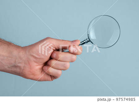 Magnifying glass lens lupe in male hand closeup over blue background 97574985