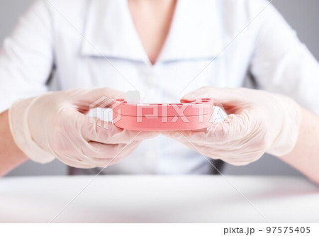 Dentist holding jaw model with single tooth. Implantation or teeth loss caused by no professional dental care, poor oral hygiene, gums diseases, traumas. Doctor in lab coat and in gloves Dentist holding jaw model with single tooth. Implantation or teeth loss caused by no professional dental care, poor oral hygiene, gums diseases, traumas. Doctor in lab coat and in gloves 97575405