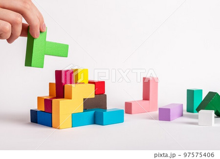Hand assembling tetris puzzle, searching appropriate place for wooden block. Construction, formation concept. Finding solution to problem. Logical thinking, reasoning strategy development. Hand assembling tetris puzzle, searching appropriate place for wooden block. Construction, formation concept. Finding solution to problem. Logical thinking, reasoning strategy development. 97575406