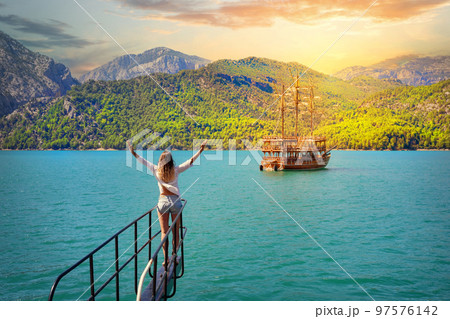 Girl with outstretched hands on bow of boat floating on azure water on sunset Girl with outstretched hands on bow of boat floating on azure water on sunset 97576142