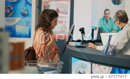 Young adult using smartwatch with nfc to pay for vitamins, standing at drugstore cash register counter. Female client paying for supplements and pills at pos terminal, pharmacy desk. 97577477