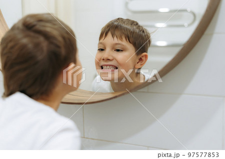 cute 8 years old boy washing face in bathroom looking in mirror and smiling.  97577853