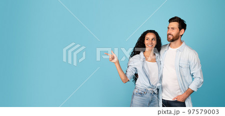 Cheerful handsome young european guy and arab lady in casual hug and point finger to empty space 97579003