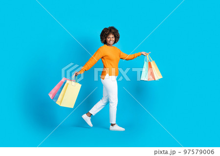 Positive carefree black woman shopaholic walking with purchases 97579006