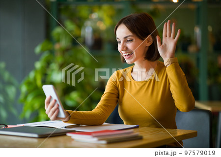 Cheerful brunette woman having video call, using phone at cafe 97579019