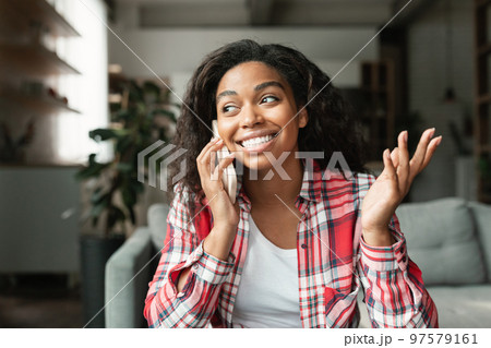 Happy pretty millennial black lady calling by smartphone, talking with friend in living room interior, close up Happy pretty millennial black lady calling by smartphone, talking with friend in living room interior, close up 97579161