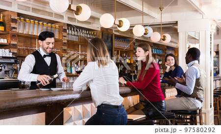 Barman is servicing young people who are relaxing in bar indoor. 97580292