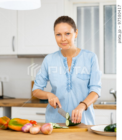 Woman cutting cucumber for salad at kitchen 97580417