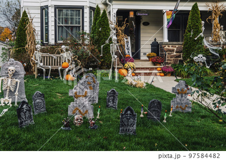 Many colorful Halloween decorations, skeletons, scarecrows at driveway and front lawn of house. 97584482
