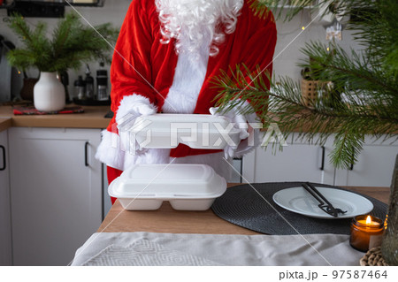 Food delivery to home service containers in hands of Santa Claus puts it on kitchen table and takes it away. Ready-made hot order, Christmas, New year holidays catering. 97587464