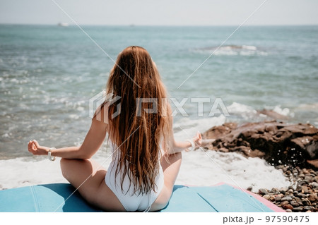 Woman yoga sea. Young woman with long hair in white swimsuit and boho style braclets practicing outdoors on yoga mat by the ocean on sunny day. Women's yoga fitness routine. Healthy lifestyle, harmony 97590475